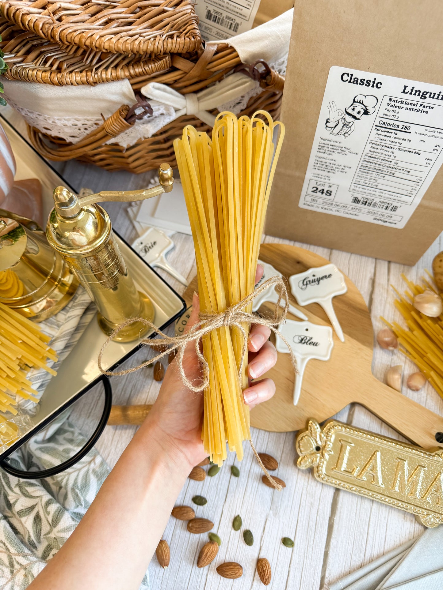Brown paper bag in the background. Hand holding a bundle of Kaslo Sourdough Linguine with decorations filling the space behind