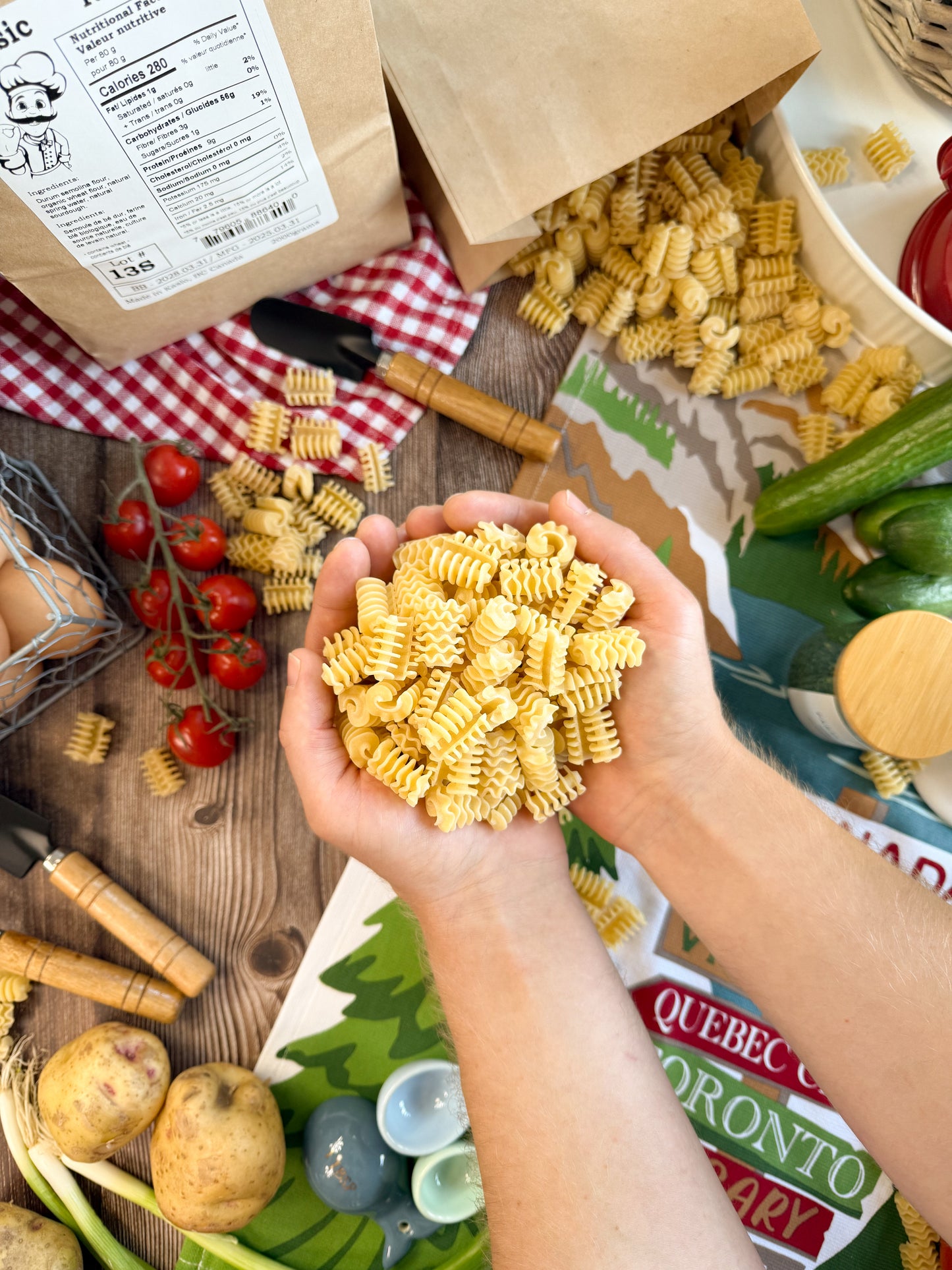 Hands holding a bunch of Kaslo Sourdough Radiatori in a lifestyle shot, with brown paper bags filled with pasta in the background