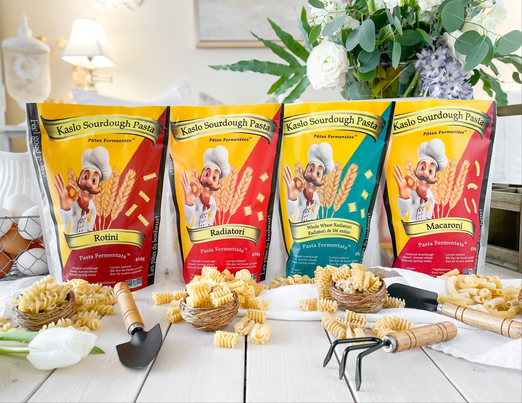 Four packages of Kalo Sourdough Pasta with pasta and gardening tools on a table.