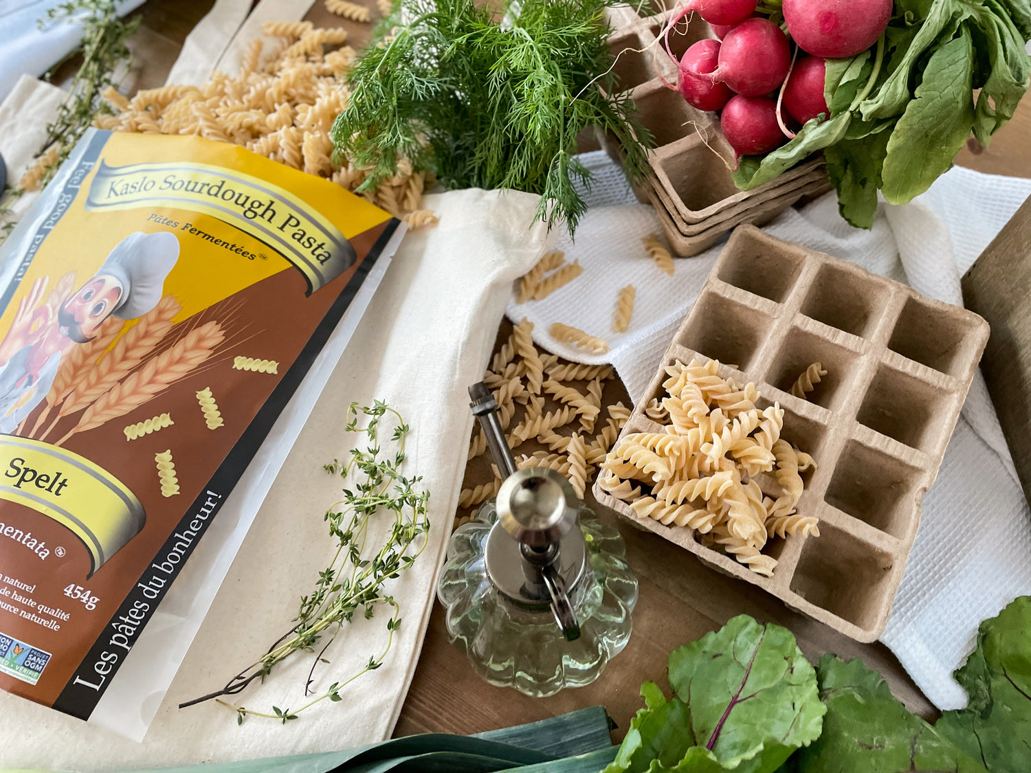 Pasta packaging with a tray of pasta and fresh vegetables on a table.